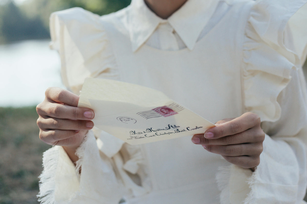 Person holding a letter with a visible postage stamp outdoors